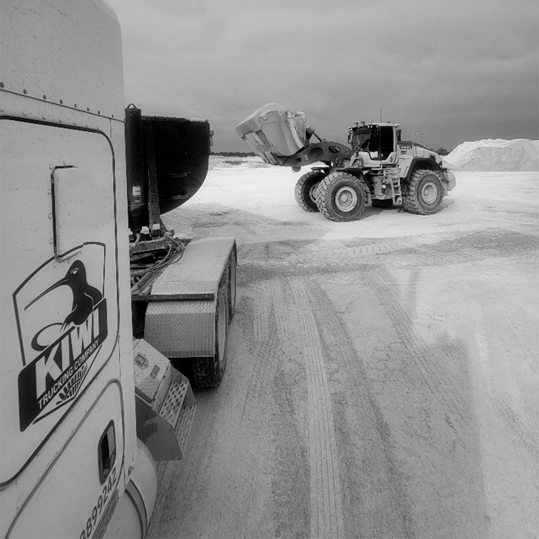 side view of KIWI truck cab being, back of truck is being loaded by dozer