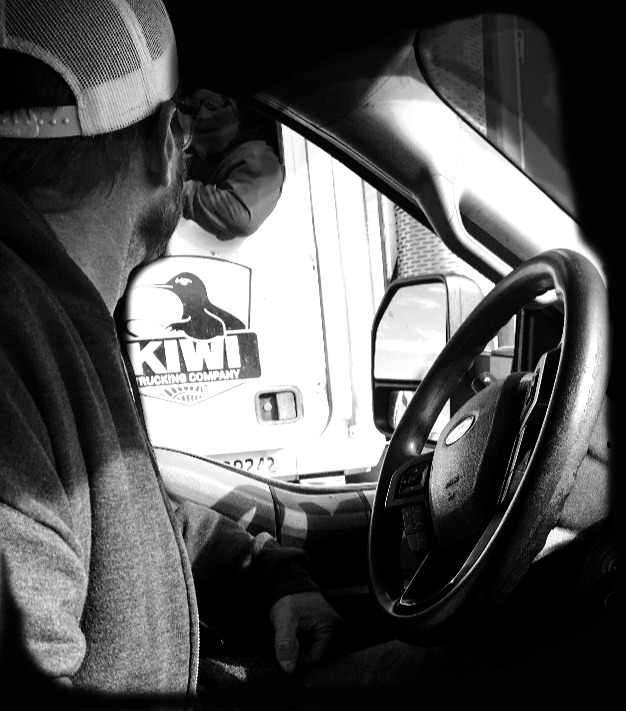 from the inside of a truck cab, looking out at another truck with "Kiwi Trucking Company" on the door